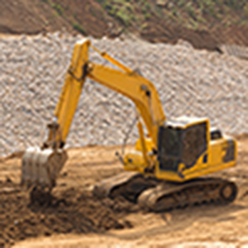 A yellow excavator at a construction site, operated by Dahme Construction in San Jose, digging in a dirt area with a gravel hillside in the background.